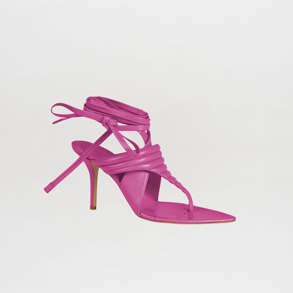 Tacones Dalila Magenta es una sandalia de tacón alto con punta puntiaguda de color rosa brillante, con un fino tacón de aguja y largas tiras que envuelven el tobillo, que se muestra sobre un fondo blanco liso.