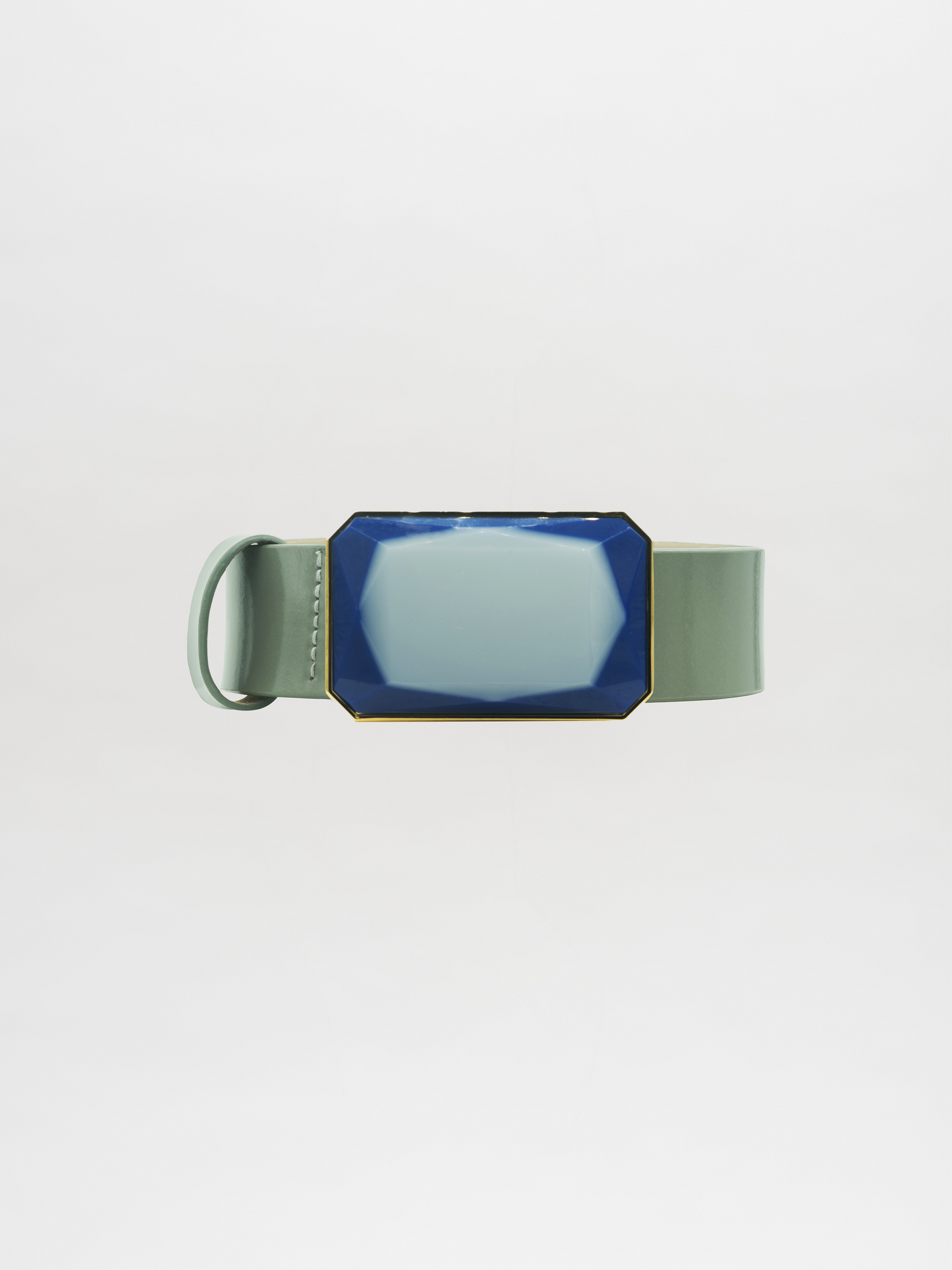 El cinturón Dora Steel Blue presenta una correa ancha de color verde salvia y una hebilla grande y geométrica de color azul acero con un contorno dorado, sobre un fondo blanco liso.