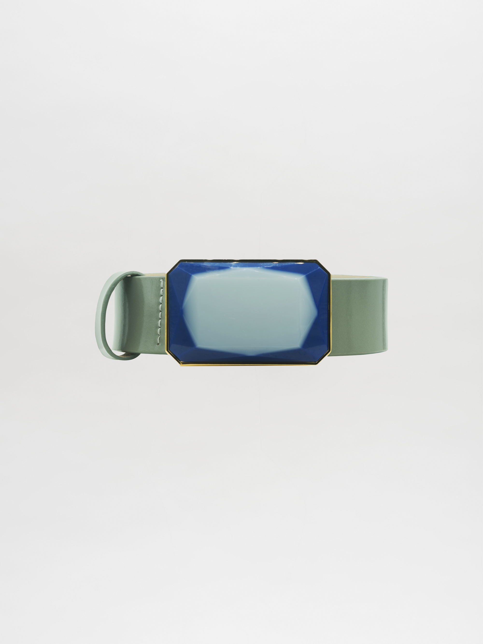 El cinturón Dora Steel Blue presenta una correa ancha de color verde salvia y una hebilla grande y geométrica de color azul acero con un contorno dorado, sobre un fondo blanco liso.