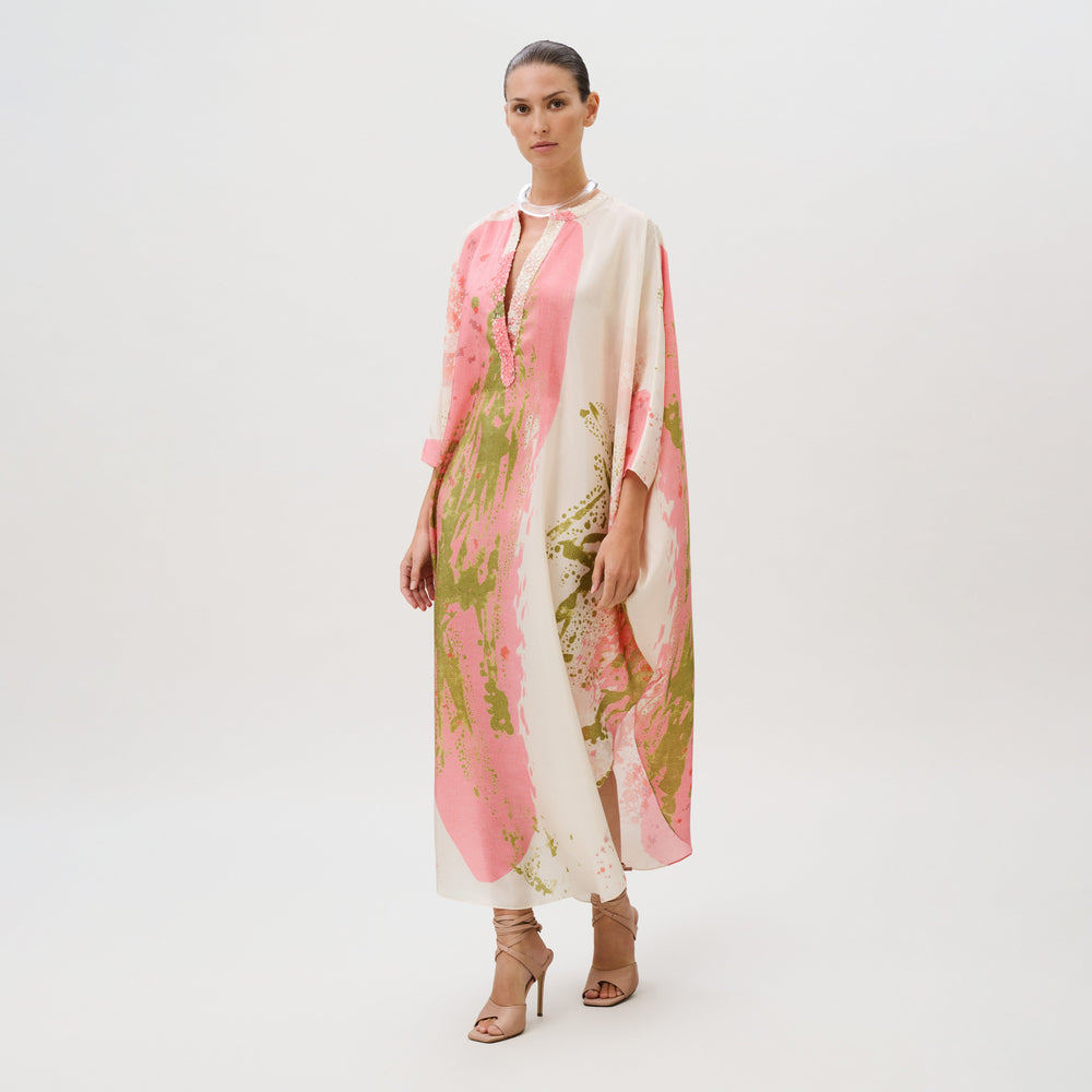 A model wearing an Elea Tunic, a loose, long-sleeved silk top with an abstract pink and green pattern, paired with lace-up heels.