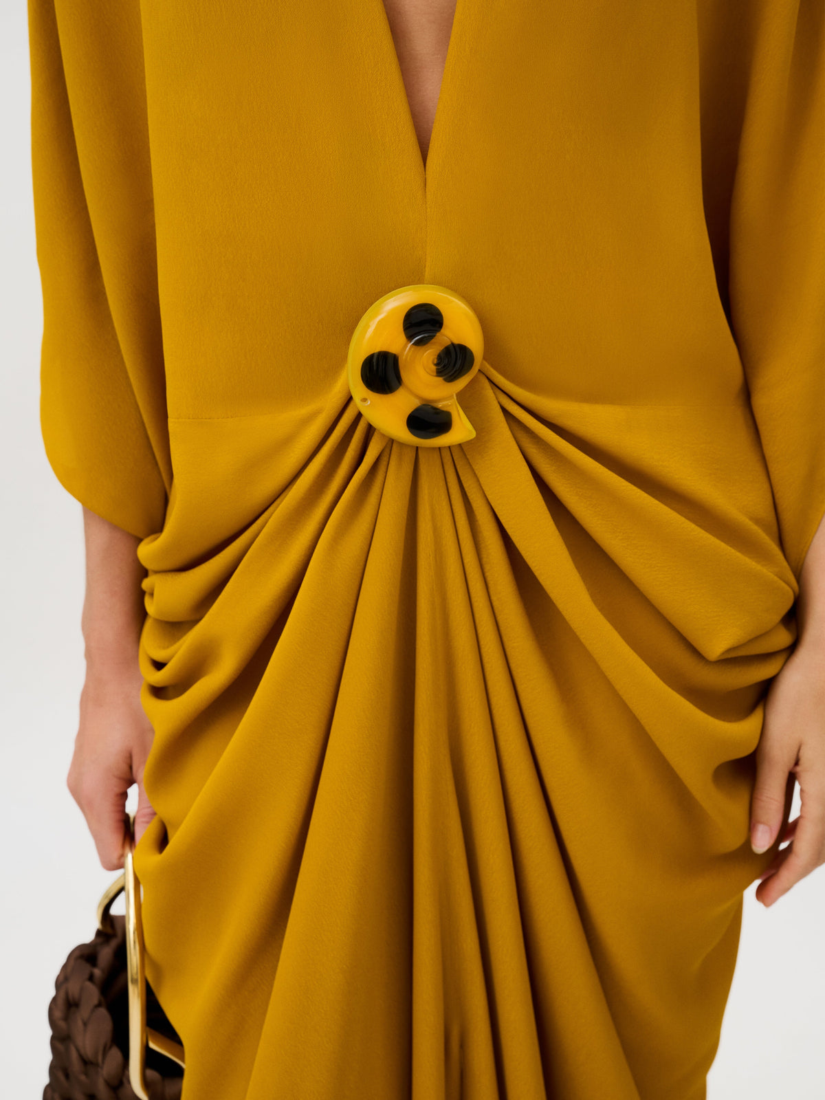 Fiore Tunic in mustard yellow Italian fabric, featuring a deep V-neck and a large, circular yellow and black abstract brooch that gathers the fabric at the waist.