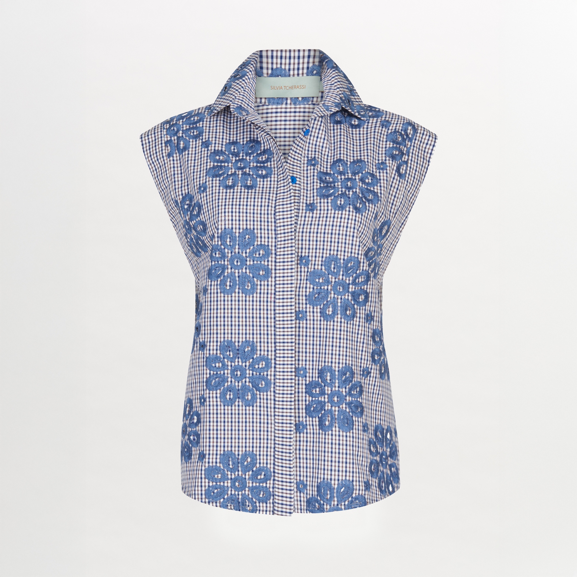 Blusa Fosca Navy Floral: blusa abotonada sin mangas con estampado floral a cuadros azules y blancos, grandes motivos florales marinos y cuello en punta, sobre fondo blanco liso.