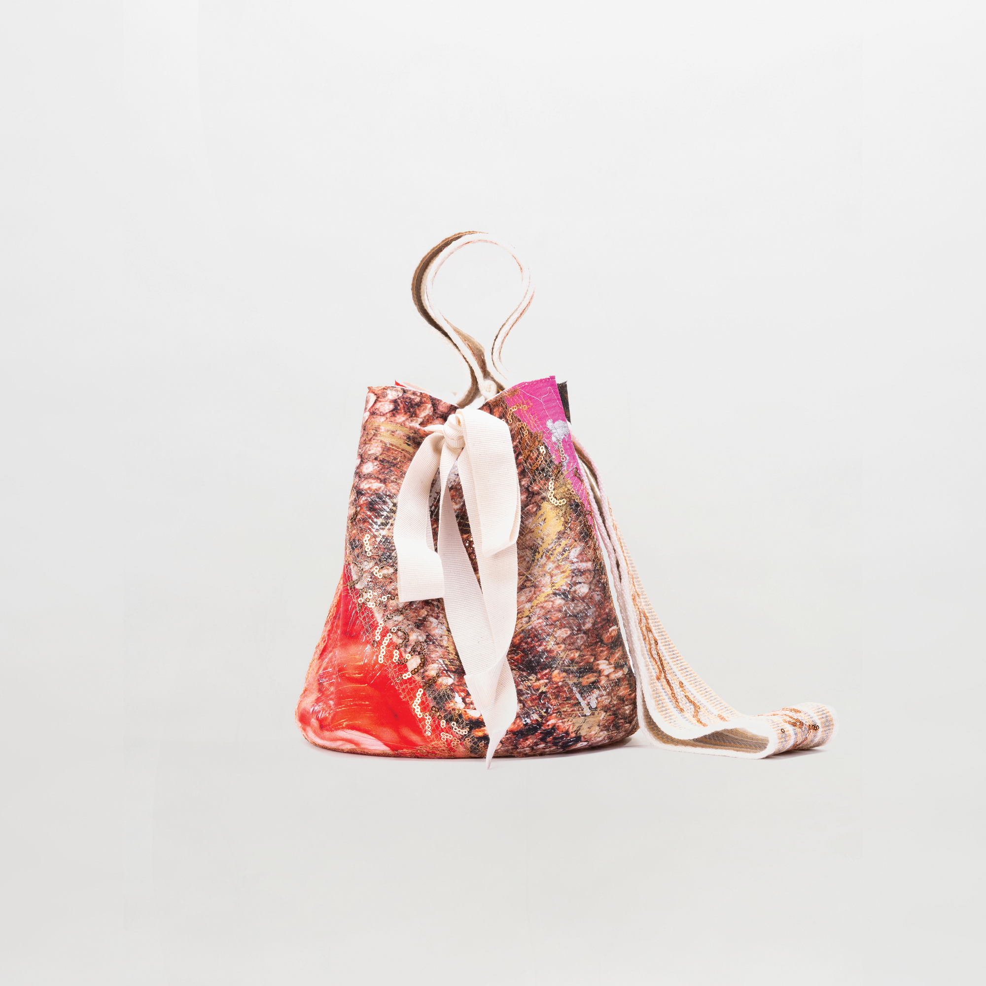 Mochila Laaput Small es un bolso tipo cubo con motivos abstractos multicolores, una correa de tela beige y un ligero lazo atado en el lateral, que se muestra sobre un fondo blanco liso.