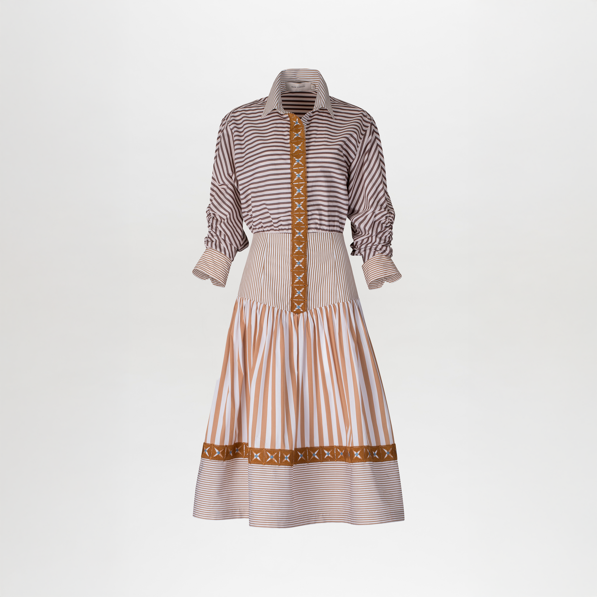 El Vestido Lamar es un vestido camisero de manga larga con estampado multicolor de rayas marrones y blancas, decorado con encaje guipur naranja en puños, botonadura, cintura y bajo. La falda lleva un elegante fruncido en la cintura.