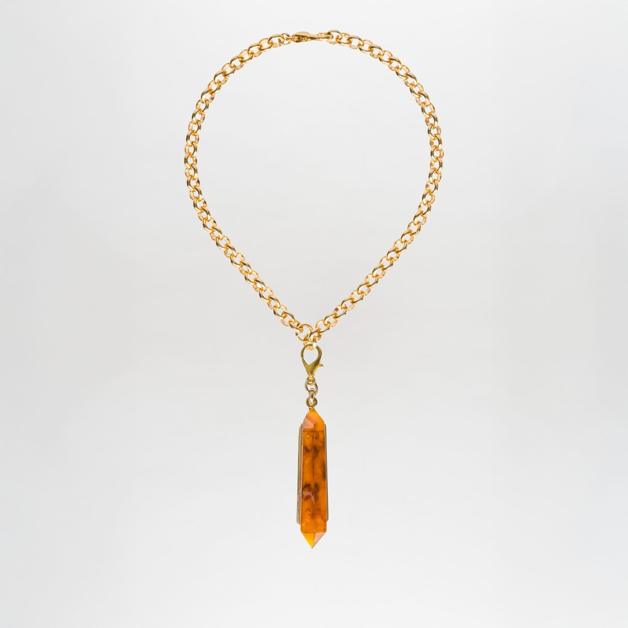 Collar Mariela: gargantilla de latón bañado en oro con colgante de cristal ámbar y gran punta central, presentado sobre fondo blanco sencillo.