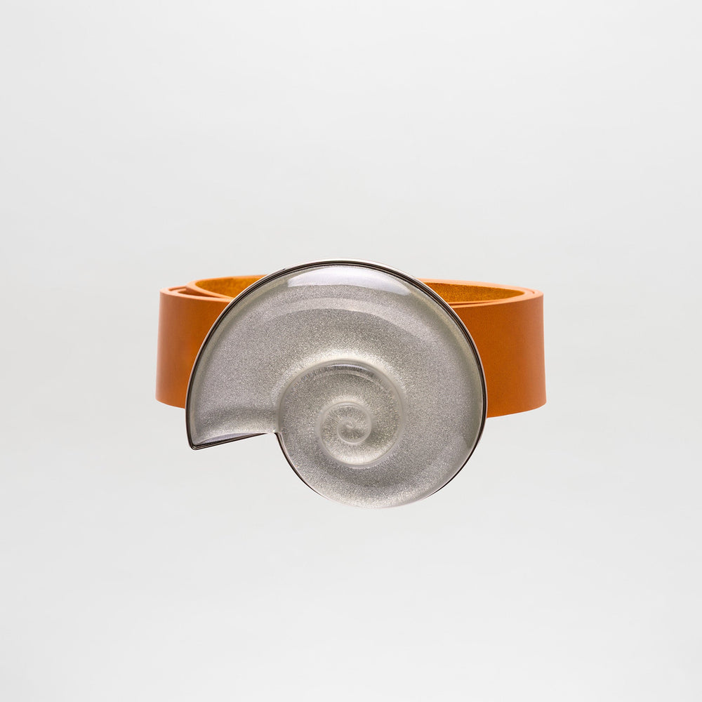 El Cinturón Nautilus, un atrevido accesorio naranja con una gran pieza central metálica en espiral inspirada en una concha de nautilo, hecho en Colombia, se muestra sobre un fondo liso gris claro.
