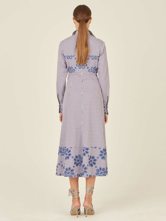 The Ganzoni Dress Navy Floral is a long-sleeve, button-down dress with a collar, featuring a blue and white checkered pattern and blue floral designs. This item is part of our Final Sale and is not eligible for return or exchange.