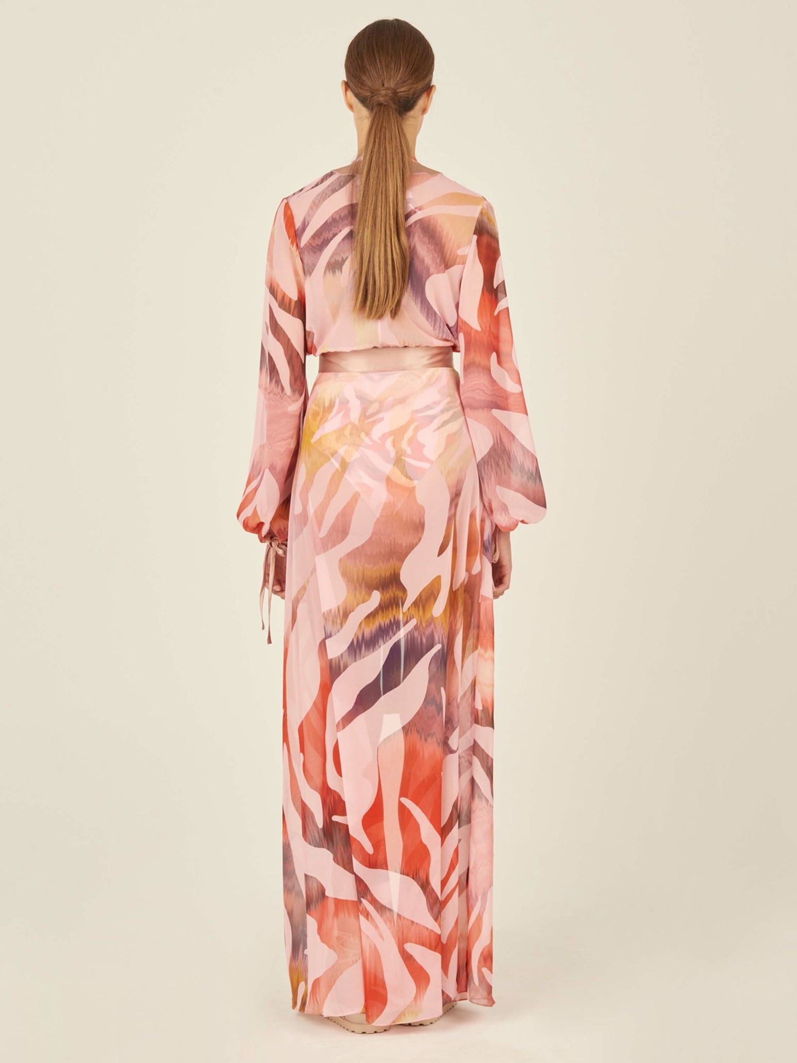 Long-sleeved, pink, and beige patterned robe with a sash belt and wide lapels. The Magdalena Dress Blush Prismatic features abstract zebra print brushstroke designs and tie detailing on the sleeves.