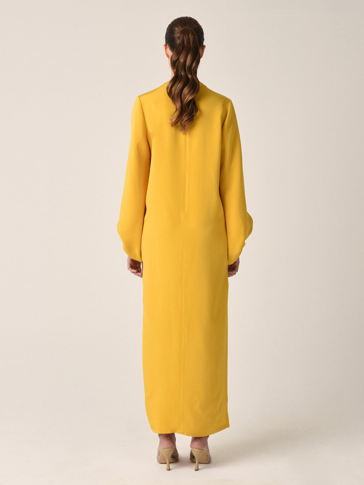 The Monferrato Tunic Amber is a long, mustard yellow dress with a high neckline and romantic balloon sleeves gathered at the wrists, featuring a small V-cut at the front. Perfect for Resort 2023, this amber-hued crepe tunic adds an elegant touch to your vacation wardrobe.