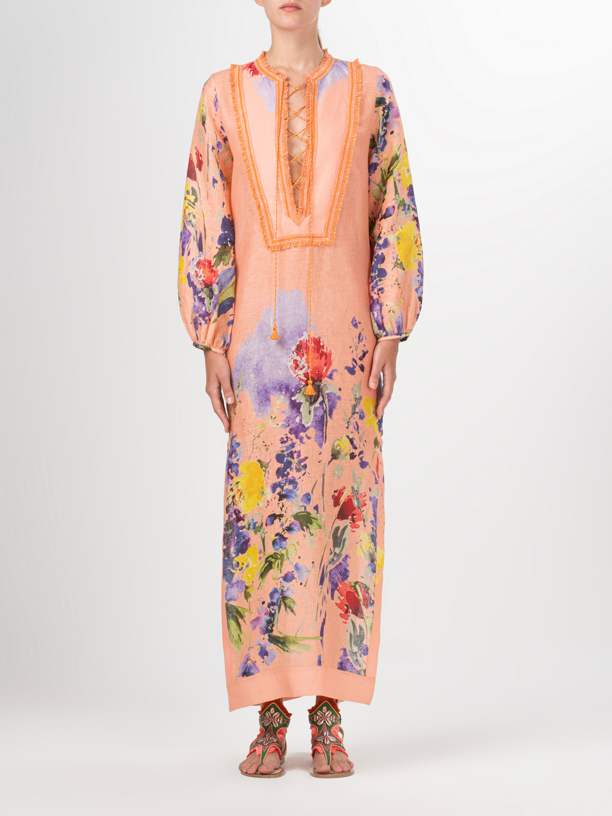 A long-sleeved, peach-colored Isernia Tunic Apricot Spring Garden with a floral pattern and fringe lace detailing on the chest. The tunic features vibrant flowers in various colors, including red, yellow, and purple.