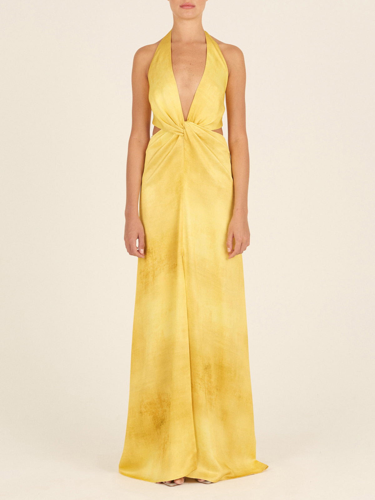 The Camila Dress Canary is a long, backless dress featuring a halter neck design in canary-hued fabric, complete with a knot detail at the front that accentuates a feminine silhouette.