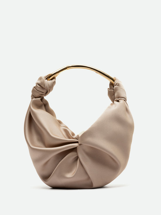 El Bolso Sofia Beige (Pequeño) es un bolso de mano de satén beige con herraje dorado, que presenta un diseño de tela trenzada y fruncida elaborado con textil italiano. Tiene un asa dorada anudada elegantemente unida en la parte superior y está orgullosamente hecho en Colombia, exhibido sobre un fondo blanco roto que rezuma sofisticación.