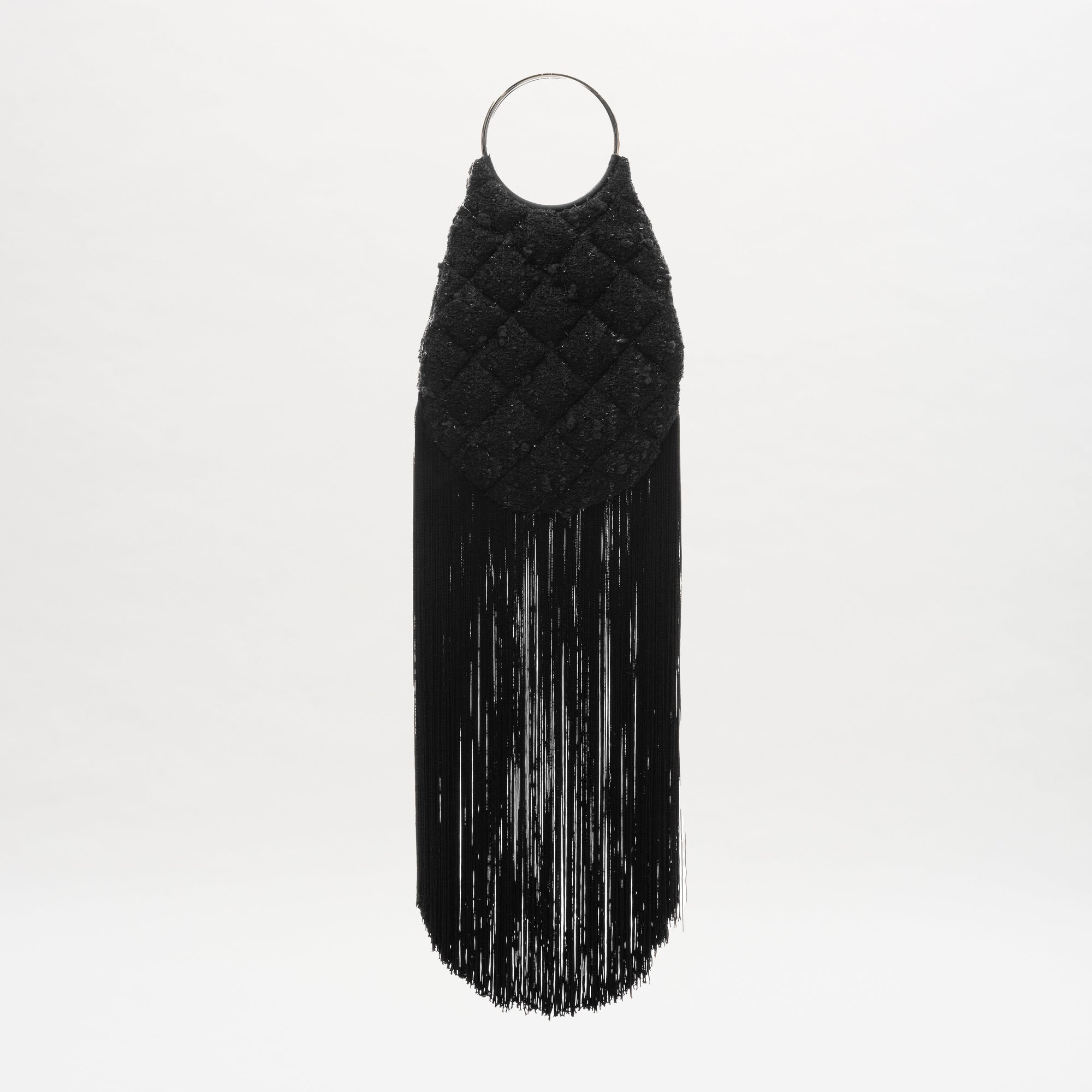 El bolso Toblach es un bolso negro de algodón con asa circular de metal, parte superior acolchada y flecos largos y finos en la parte inferior, todo ello sobre un fondo blanco liso.