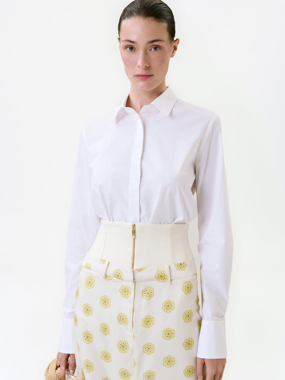 A person wearing a Yemi Shirt tucked into cream-colored trousers with a wide, zippered waistband and a repeating yellow geometric pattern.