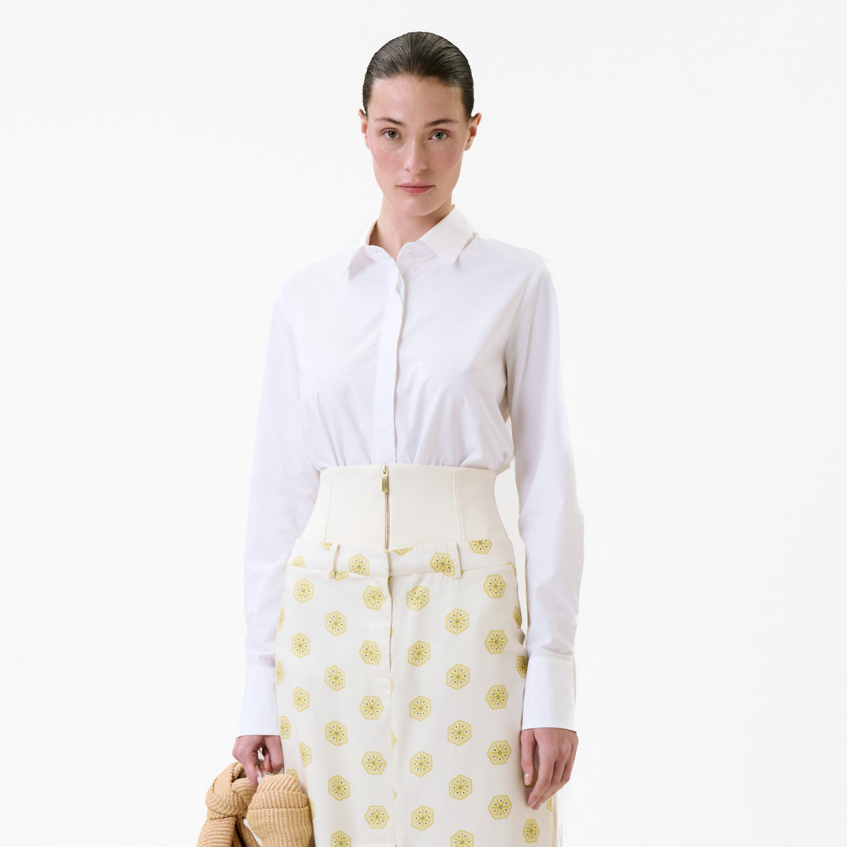 A model wearing a white long-sleeved Yemi Shirt tucked into high-waisted patterned trousers with a wide band and a front zipper.