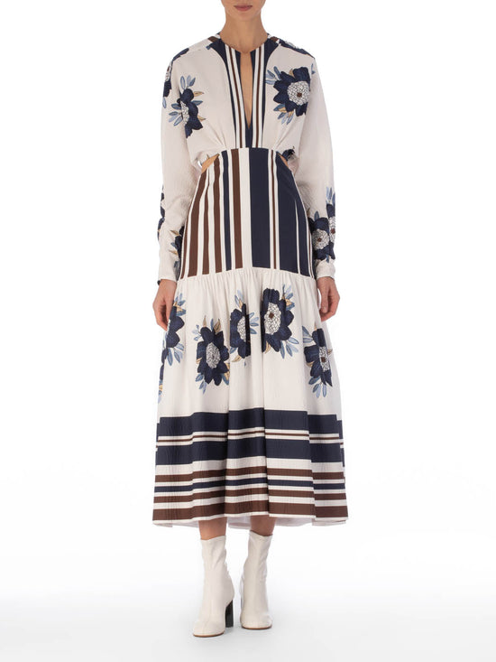 A long-sleeved Gabina Dress Multi Navy Brown Floral featuring a white base with blue floral patterns and horizontal navy stripes, designed with a flared skirt, isolated on a white background.