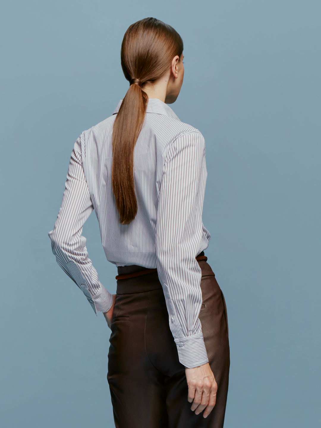 A brown-haired woman with her hair tied back is wearing the Naroa Blouse Multi Brown Stripes, featuring floral embroidery, along with brown pants. She is standing in front of a light blue background, indicating the date as August 19th, 2024.